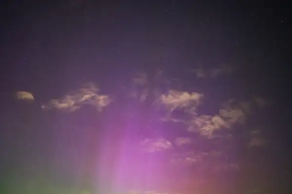 Starry night sky with faint, wispy clouds scattered across. A subtle aurora displays vertical streaks of purple and green. The scene is calm and expansive with stars dotting the background.