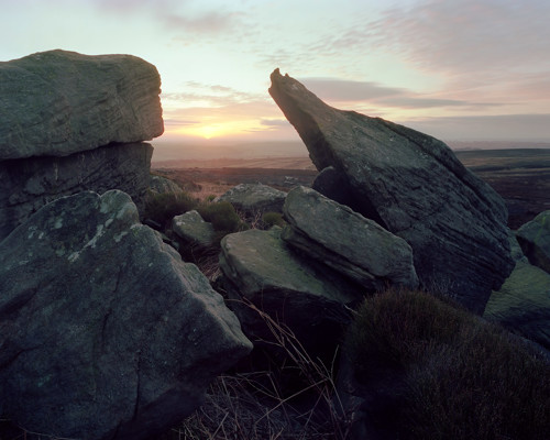 Moorland Landscapes: A twilight scene over North Yorkshire moors with rugged rocks in the foreground. A warm glowing horizon peeks through the stones, casting a gentle light over the expansive heather-clad landscape, which stretches into the distance. a view of a large rock