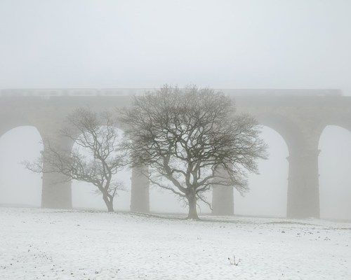 Crimple Valley Viaduct: A Marvel of Engineering and Beauty: A train passes over the Crimple Valley Viaduct on a cold winter day  a building covered in snow