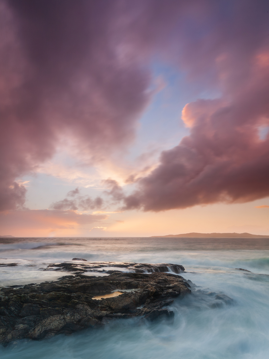  a rocky beach with a pink and blue sky