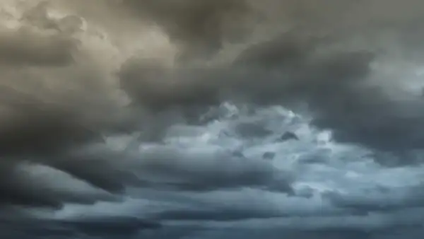 Dense dark clouds fill the sky, creating a dramatic and moody atmosphere. The clouds are layered, with varying shades of grey and blue, conveying an impending storm. The light seems dim, enhancing the contrast and depth of the cloud formations.
