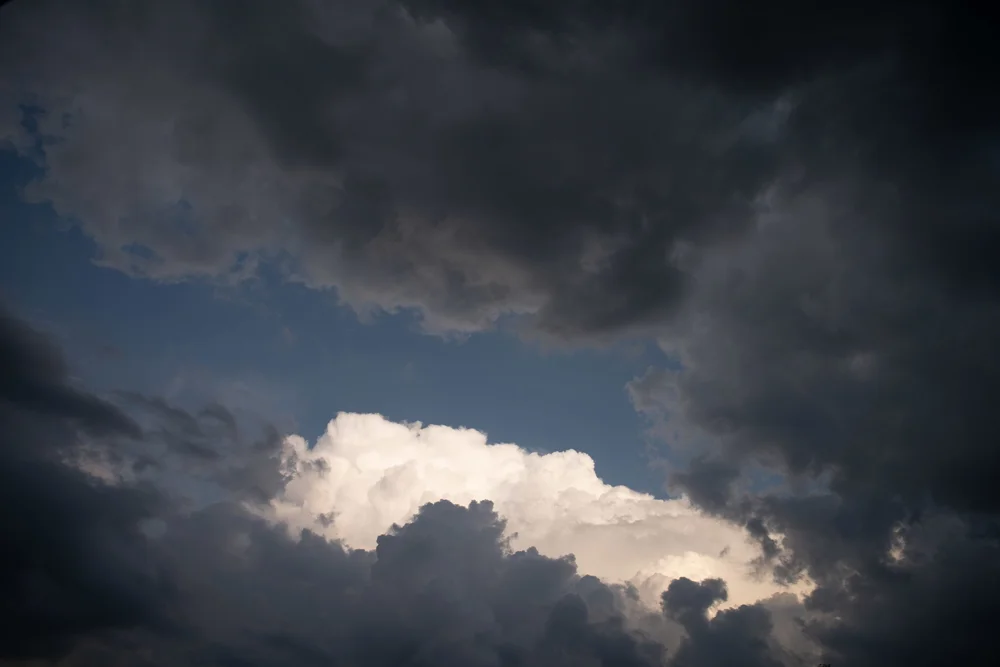 Sunlit cumulus cloud breaking through dark storm clouds against a patch of blue sky