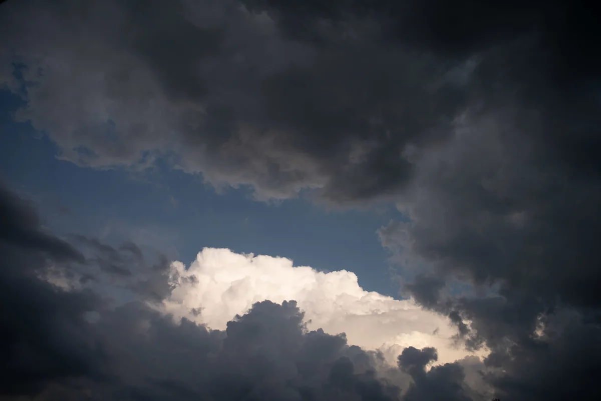 Sunlit cumulus cloud breaking through dark storm clouds against a patch of blue sky