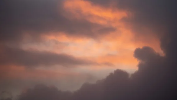 Glowing orange and grey storm clouds at sunset filling a dramatic evening sky