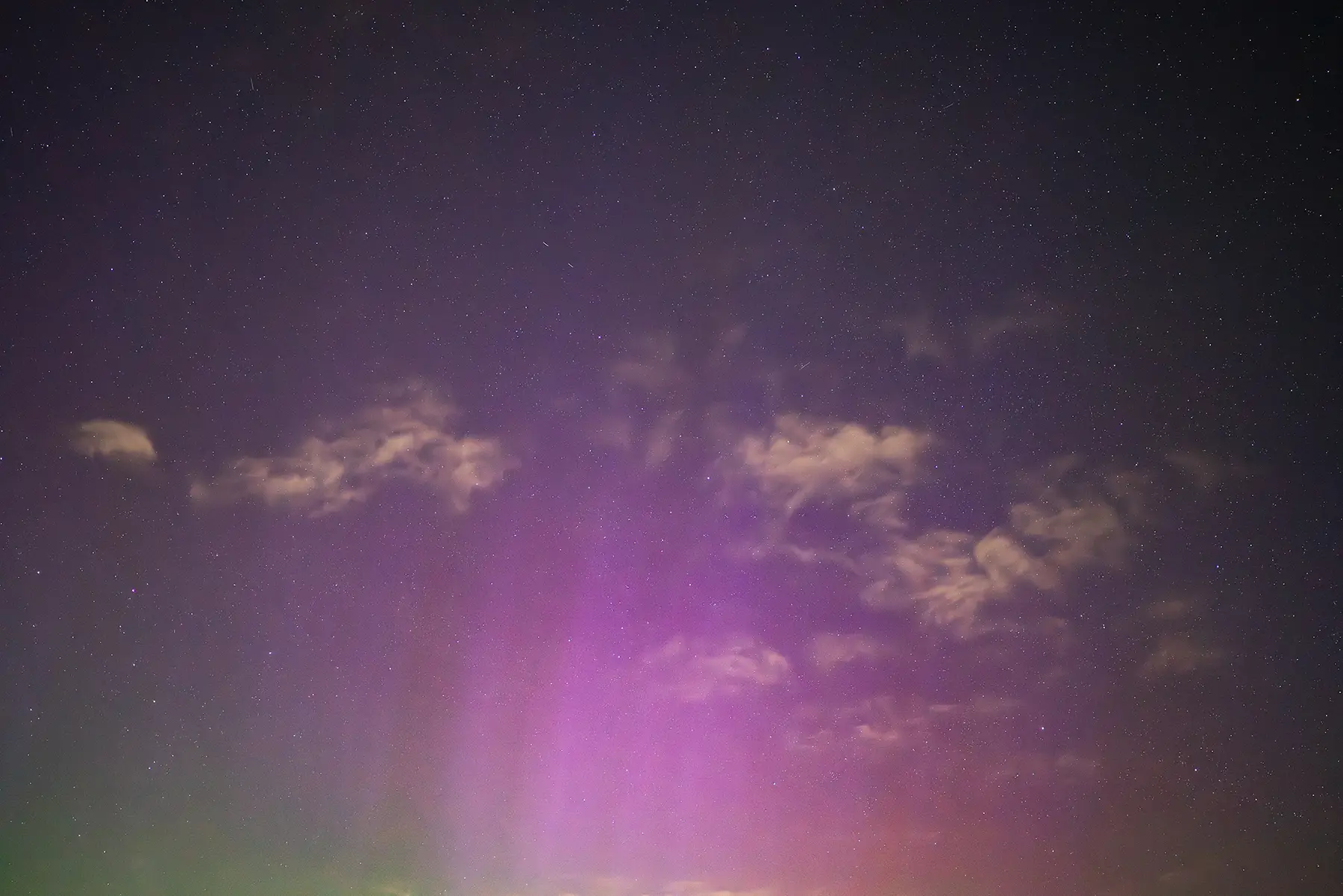 Pink and purple aurora borealis with rising light pillars beneath a starry night sky scattered with cloud