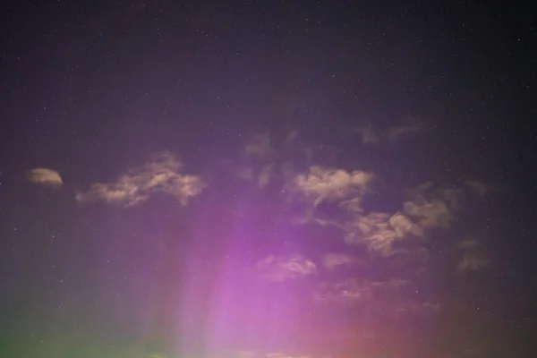 Pink and purple aurora borealis with rising light pillars beneath a starry night sky scattered with cloud
