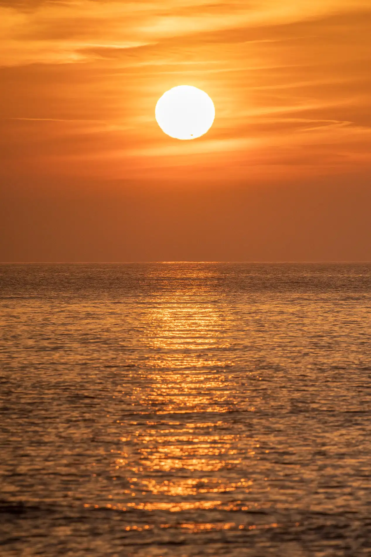 Golden sun low over a calm sea at sunset, casting a shimmering orange path across the rippled water