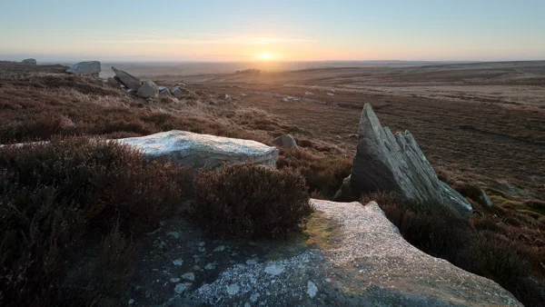 Lichen-covered gritstone boulders on open moorland at sunrise, with frost and golden light across heather