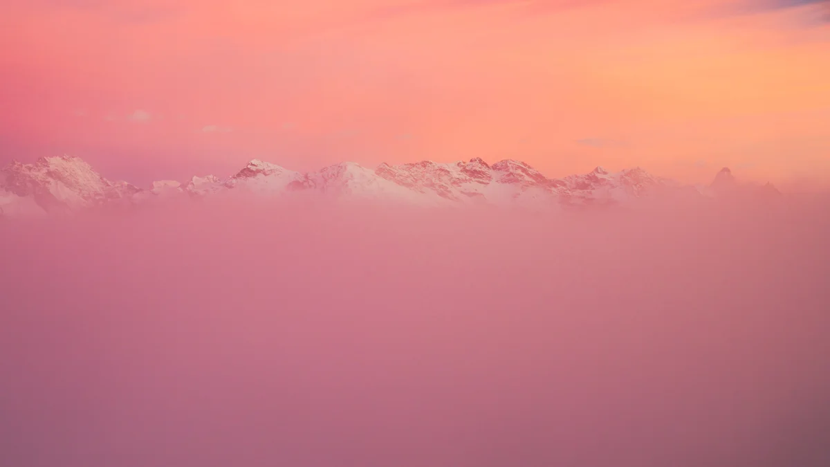 Snow-capped mountain peaks emerging from soft pink mist at sunrise