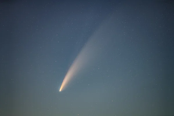 Comet Neowise with bright glowing tail across a star-filled twilight sky