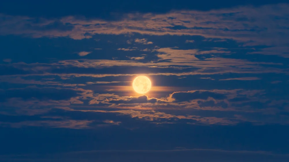 Glowing full moon rising through layered cloud in a deep blue twilight sky