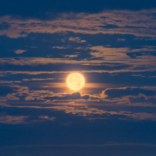 Blue Moon: A full moon emits a glowing light through scattered clouds in a twilight sky. The moon's brilliance creates a halo effect, with the clouds illuminated in soft shades of blue and orange, evoking a peaceful nocturnal scene.