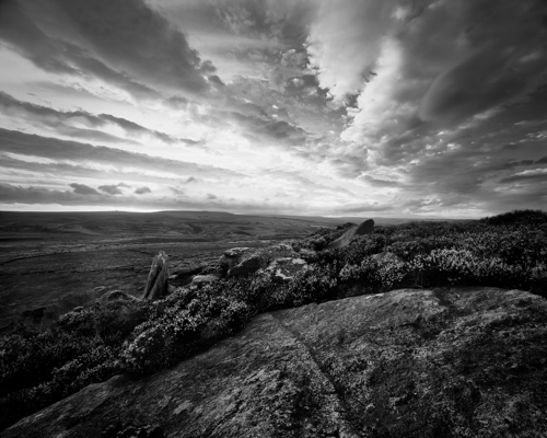 Moorland Landscapes: An atmospheric monochrome scene of North Yorkshire moorland with a dramatic sky. Foreground features rugged rocks and heather, stretching into a vast, open landscape that speaks to the wild, untamed beauty of the area. a rocky landscape with clouds
