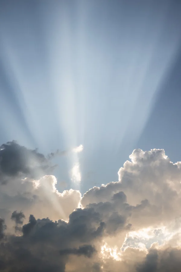 Sunbeams bursting through towering cumulus clouds against a blue sky