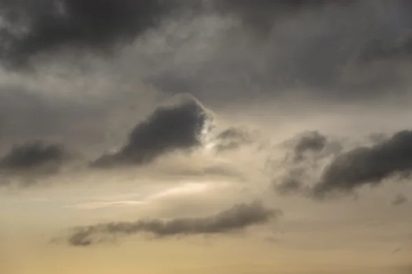 Brooding grey storm clouds breaking over a soft golden sky at sunset