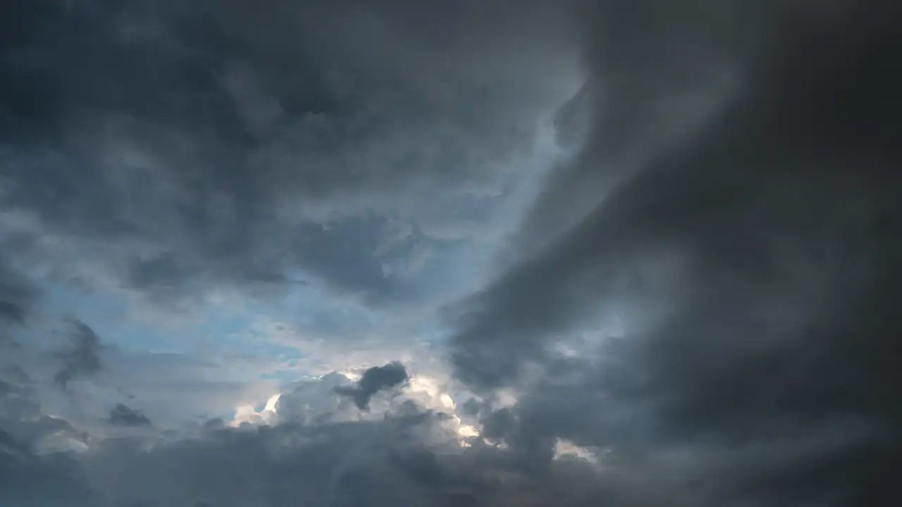 Dramatic cloudy sky with a mix of dark grey storm clouds and patches of lighter blue sky peeking through. Soft, diffused light highlights the edges of the clouds, creating a sense of depth and movement.