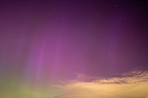 Pink and green aurora borealis with stars and low golden cloud across a dark night sky
