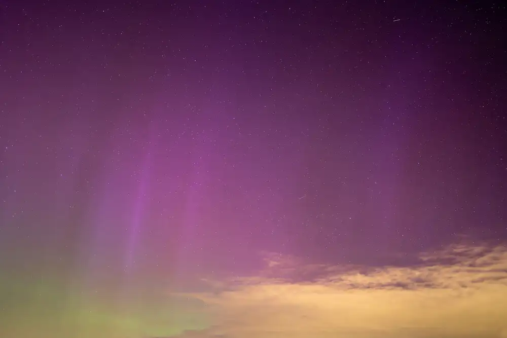 Aurora borealis displaying vibrant purple and green hues across the night sky, with stars scattered throughout and wispy clouds illuminated by the colourful glow near the horizon.