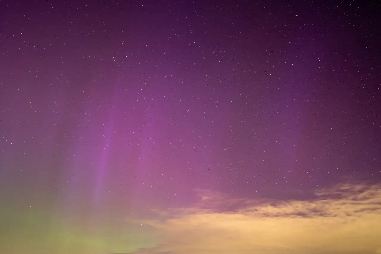 Aurora borealis displaying vibrant purple and green hues across the night sky, with stars scattered throughout and wispy clouds illuminated by the colourful glow near the horizon.