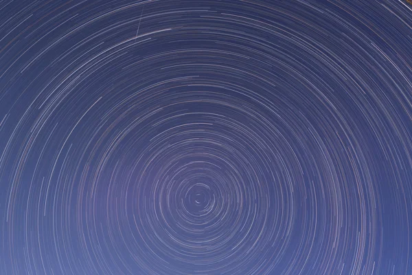 Circular star trails spiralling around Polaris in a deep blue night sky during a long-exposure astrophotography session