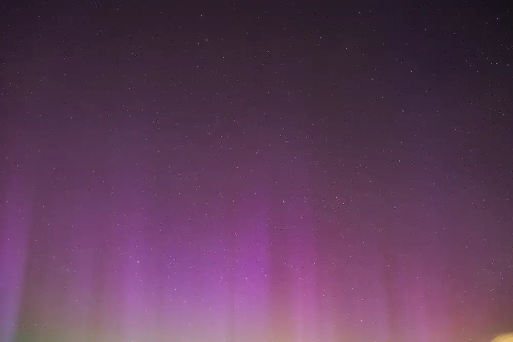 Purple aurora borealis lights the night sky with vertical streaks, set against a backdrop of numerous small stars scattered throughout. The horizon features a subtle green glow.