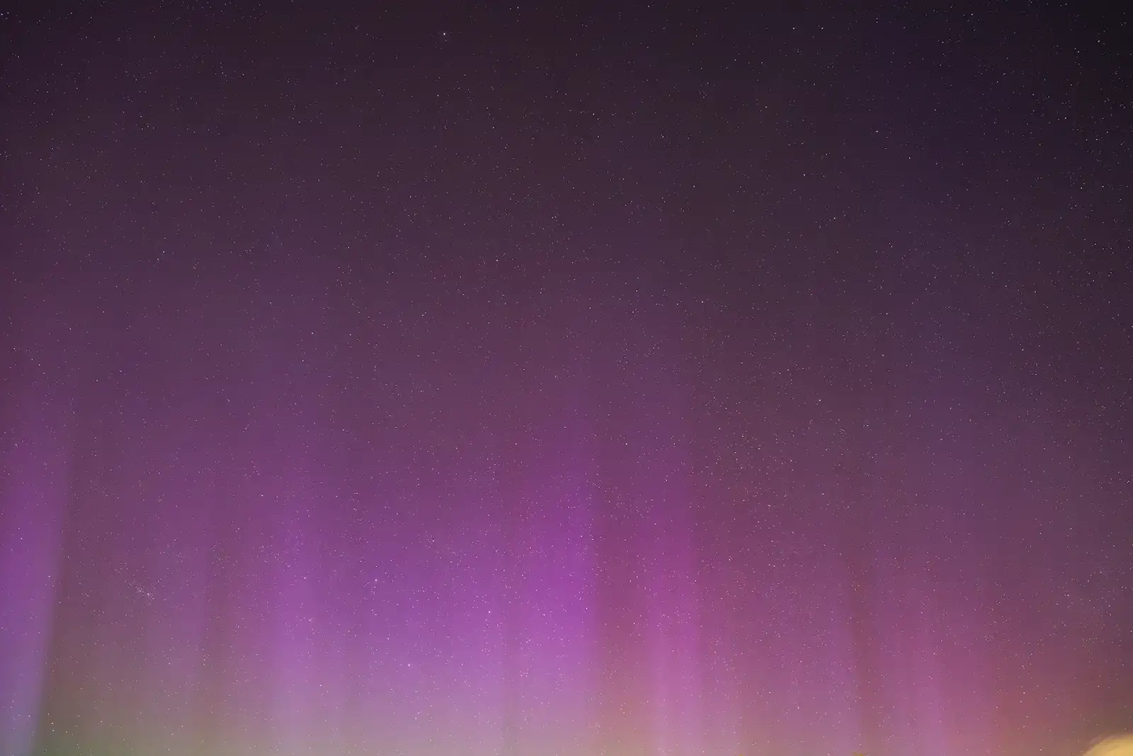 Purple aurora borealis lights the night sky with vertical streaks, set against a backdrop of numerous small stars scattered throughout. The horizon features a subtle green glow.
