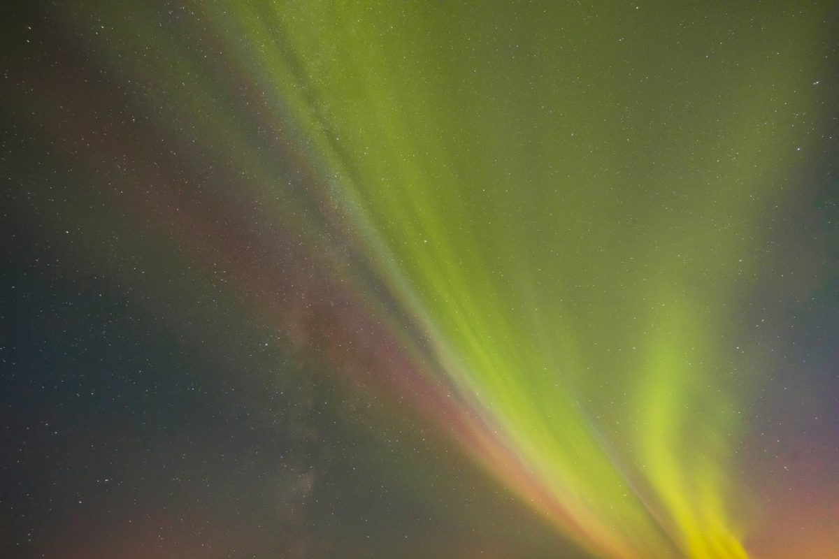 Aurora Borealis in Iceland's night sky. Vivid streaks in shades of green and pink create a curtain-like effect against the dark, star-speckled backdrop. a rainbow in the background