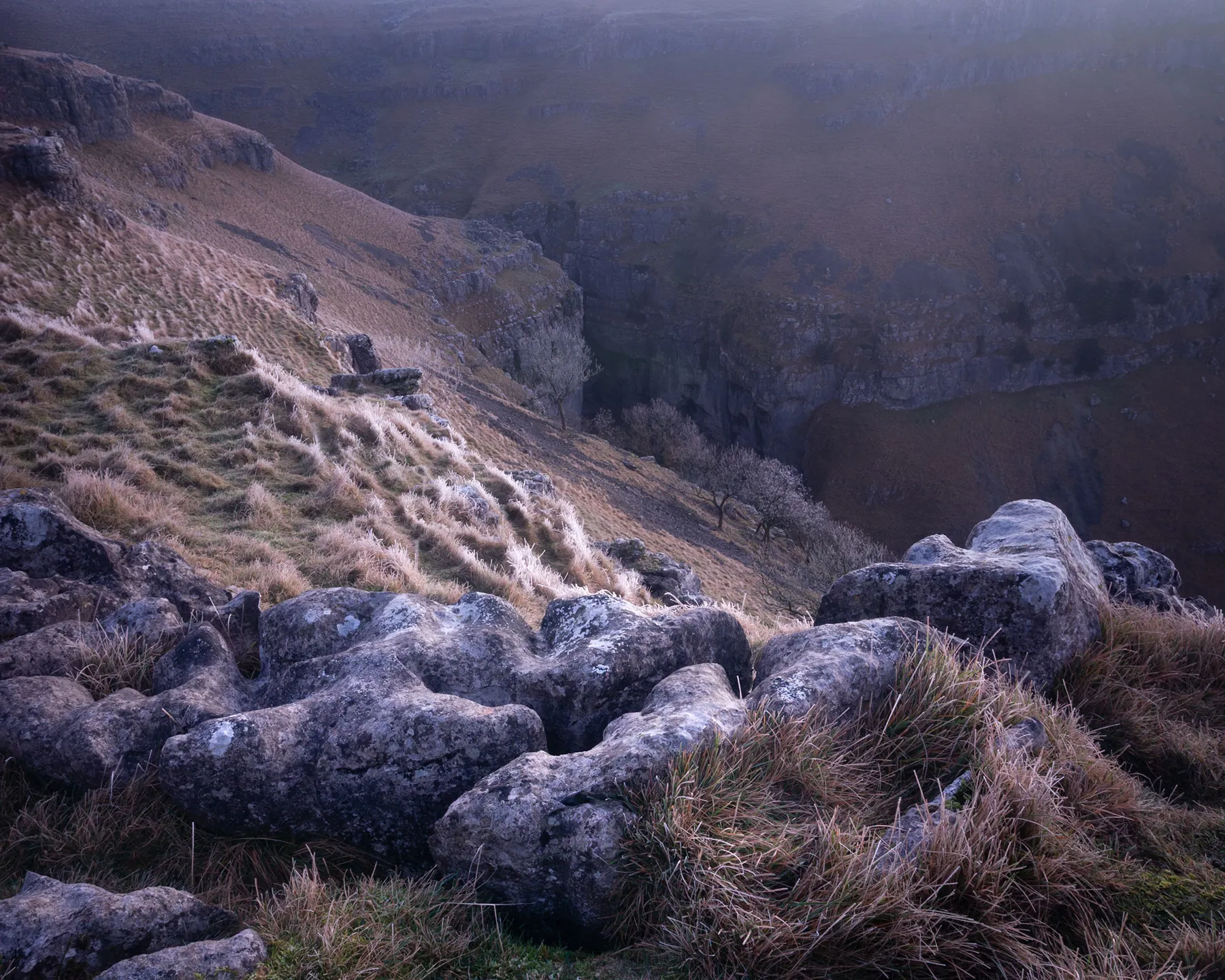 Rocky moorland foreground overlooking misty valley with forested slopes and distant hills in Yorkshire Dales.