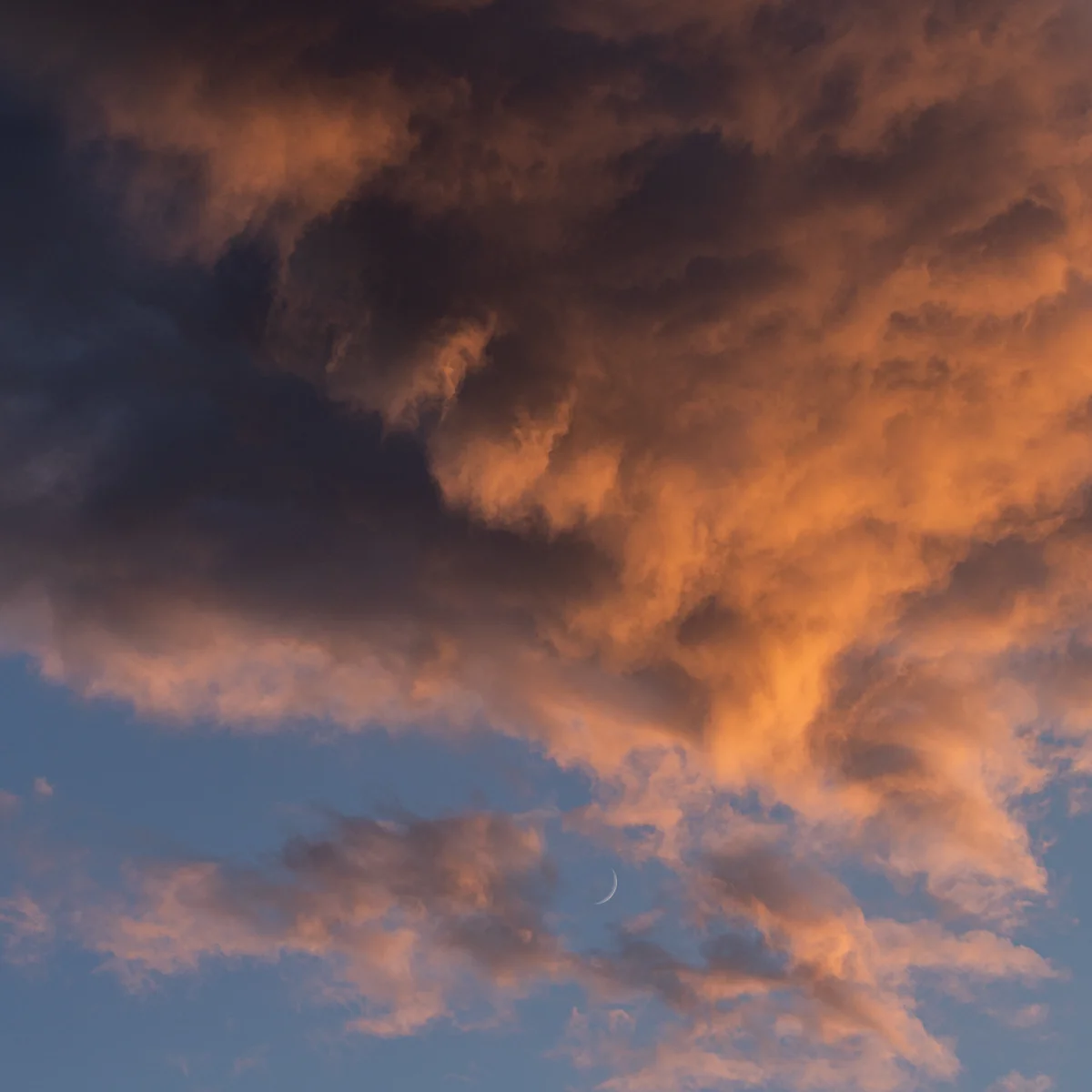 Crescent moon framed by glowing orange sunset clouds against a deep blue sky