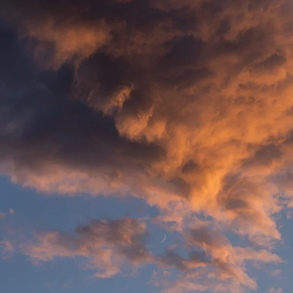 Crescent moon framed by glowing orange sunset clouds against a deep blue sky