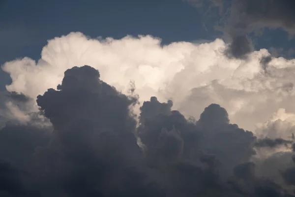 Towering cumulus storm clouds against a deep blue sky, lit by warm late-afternoon sunlight.