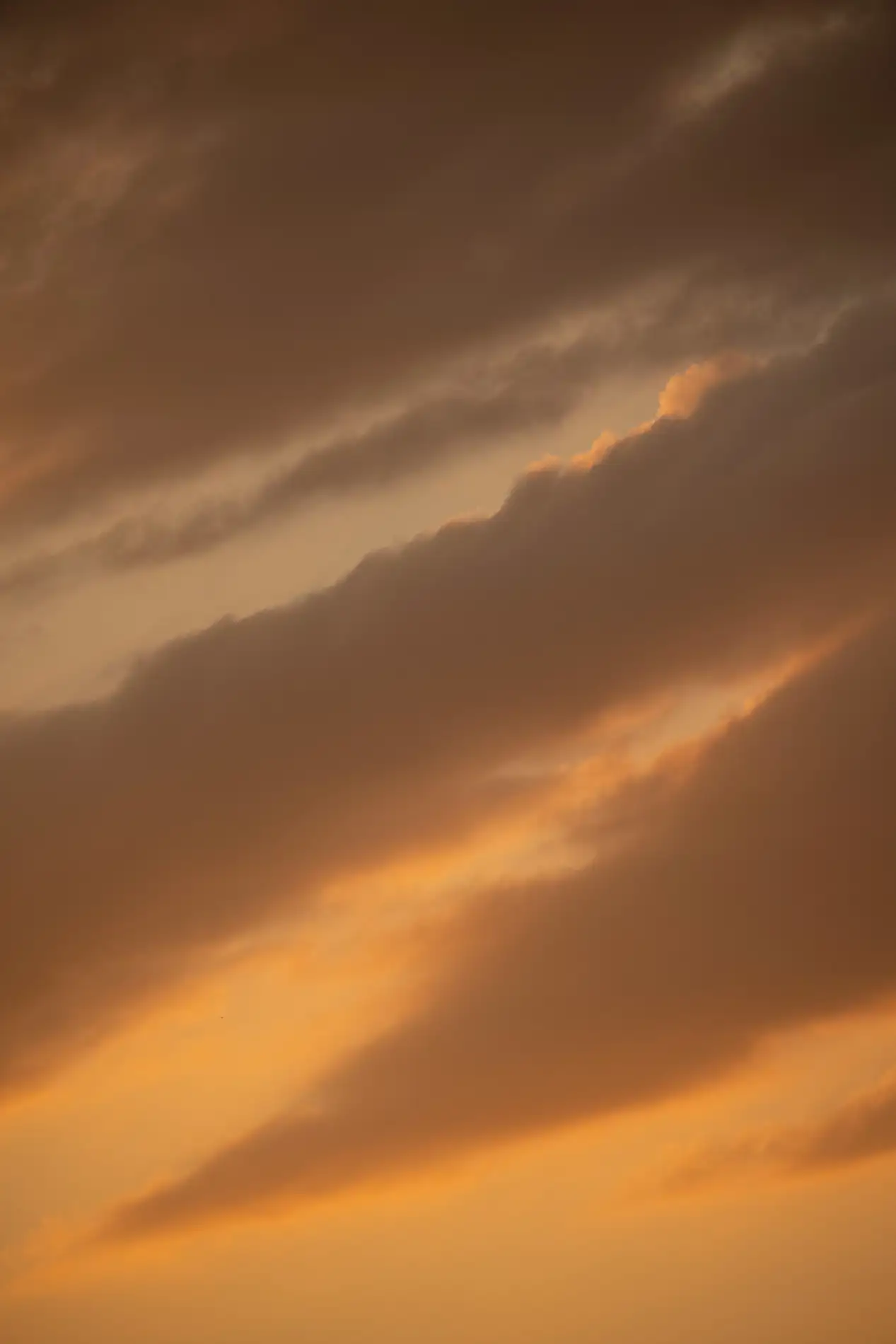 Layered amber and grey clouds glowing at sunset across a warm-toned sky