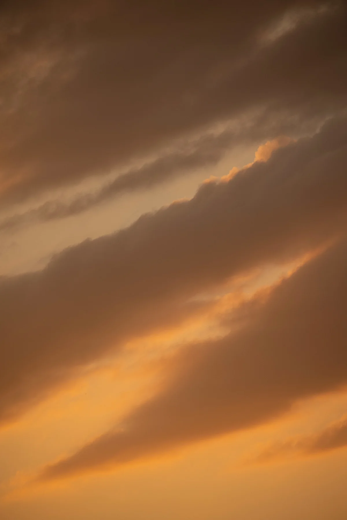 Layered amber and grey clouds glowing at sunset across a warm-toned sky