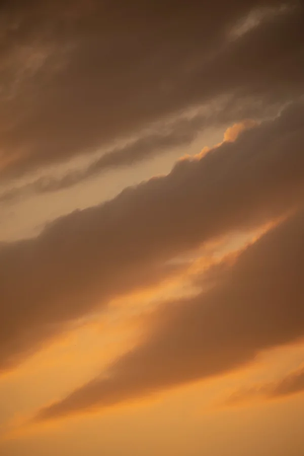 Layered amber and grey clouds glowing at sunset across a warm-toned sky