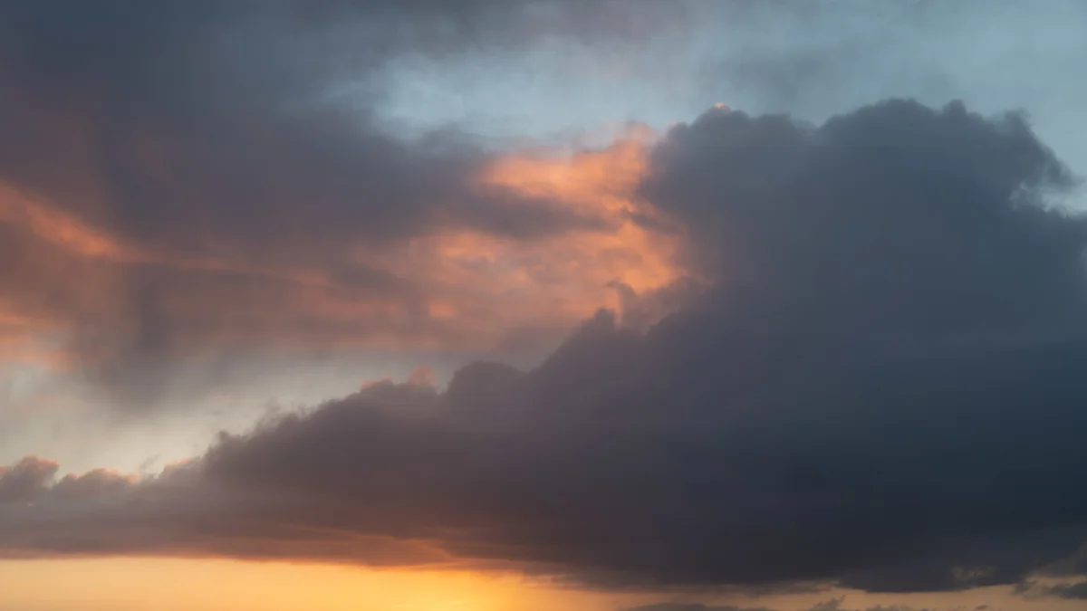 Brooding storm clouds catching warm orange light at sunset above a glowing horizon