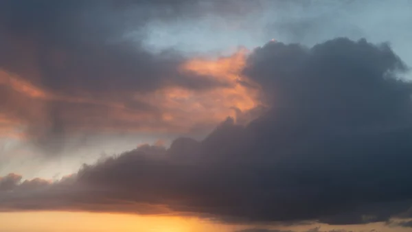 Brooding storm clouds catching warm orange light at sunset above a glowing horizon
