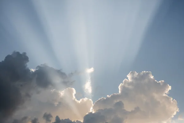 Sunbeams bursting through towering cumulus clouds against a blue summer sky