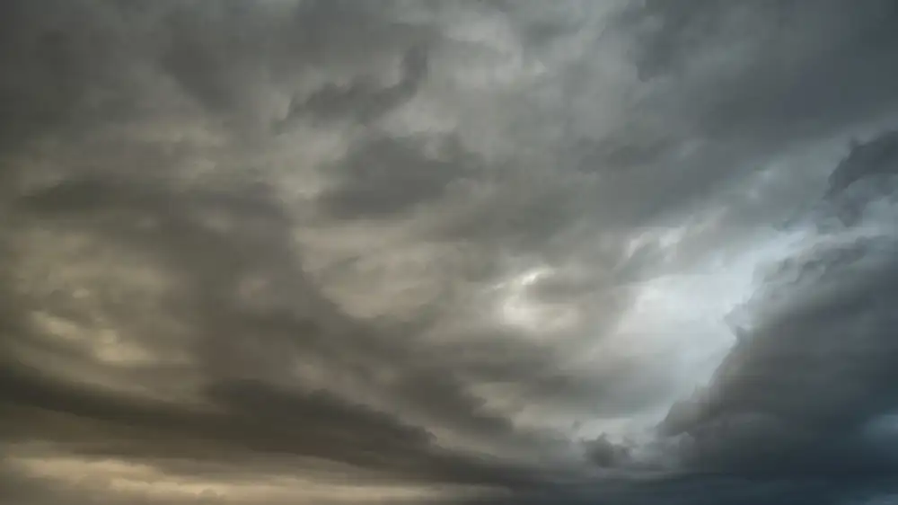 Dark, dramatic clouds fill the sky, with varying shades of grey and hints of light peeking through. The cloud formations are dense and swirling, creating a moody and atmospheric scene.