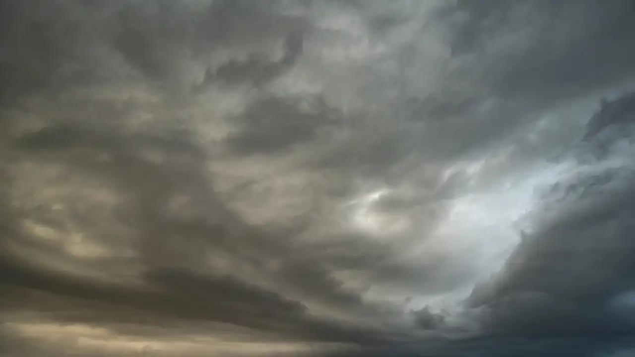 Dark, dramatic clouds fill the sky, with varying shades of grey and hints of light peeking through. The cloud formations are dense and swirling, creating a moody and atmospheric scene.