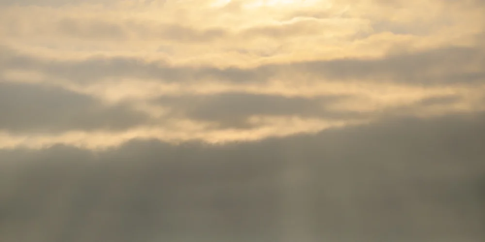 Soft golden sunlight filtering through layered cloud at dawn over a hazy horizon